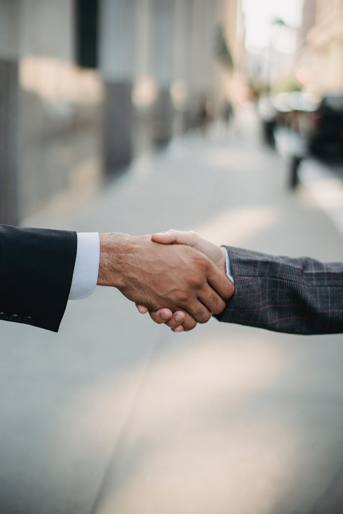 Two businessmen shaking hands outside, symbolizing cooperation and agreement in a city setting.